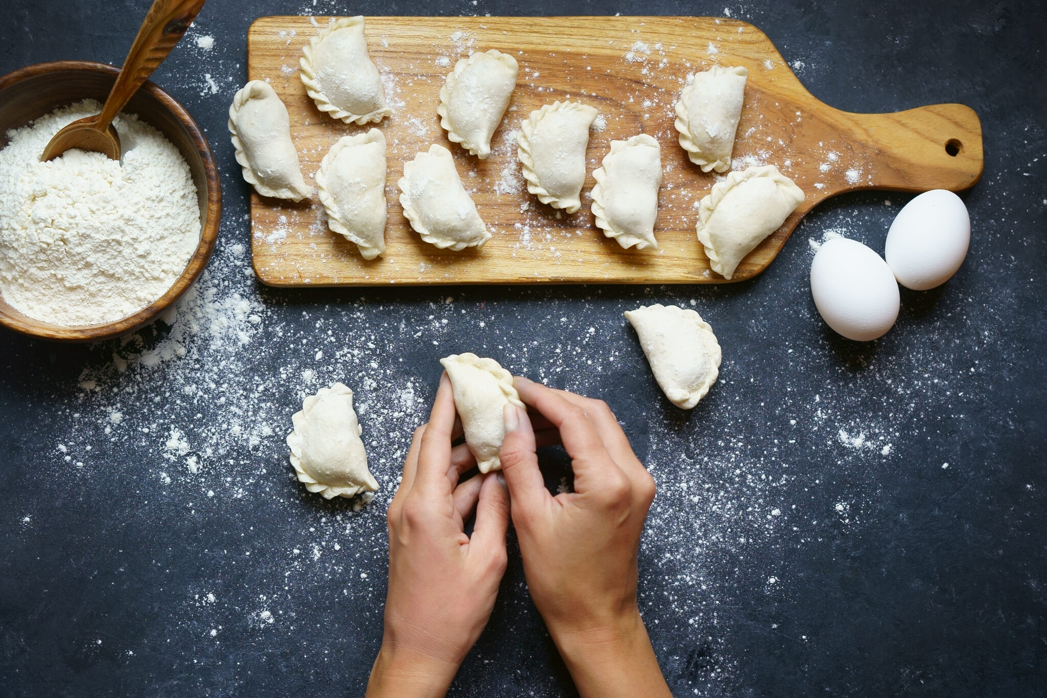 Hands pleating dumplings on a flour dusted board