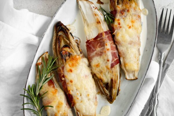 Braised chicory with ham, endives on a light stone background. Traditional Belgian cuisine.