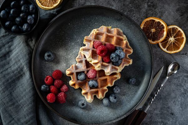 Belgian waffles with blueberries and raspberries on grey plate and dark background