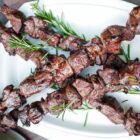 Skewers of grilled lamb garnished with rosemary on a white platter