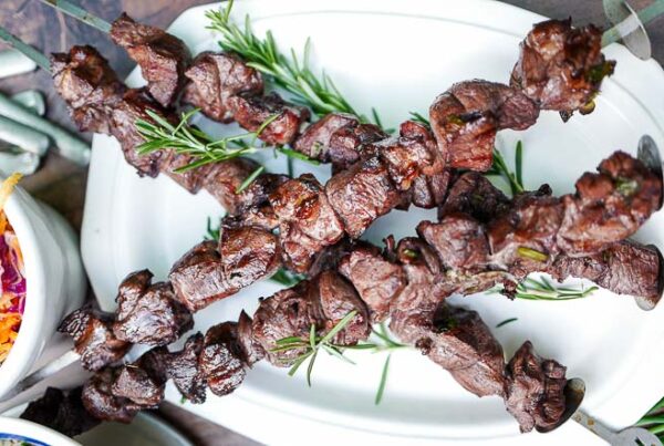 Skewers of grilled lamb garnished with rosemary on a white platter