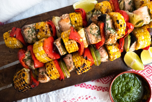 3 skewers of corn and salmon shashlik on a wooden cutting board