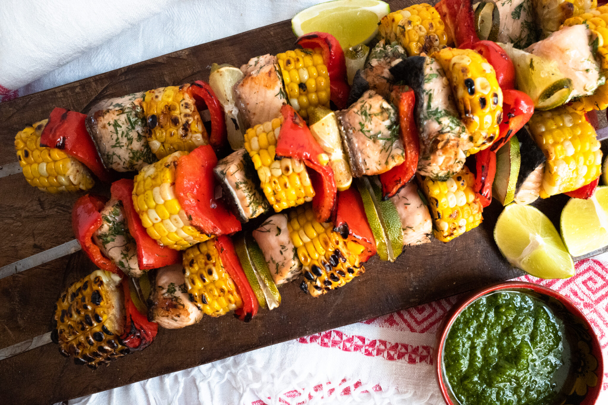 3 skewers of corn and salmon shashlik on a wooden cutting board