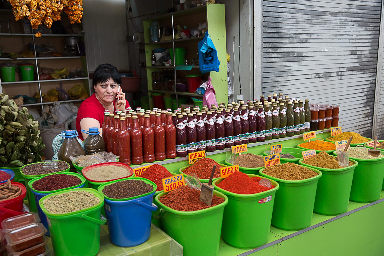 buckets of loose spices and bottles of sauce on sale at a Tbilisi Market